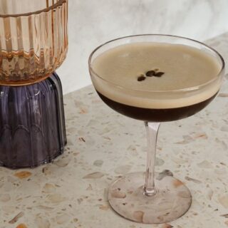 Vegan espresso martini with foam and coffee beans – cocktail on terrazzo countertop