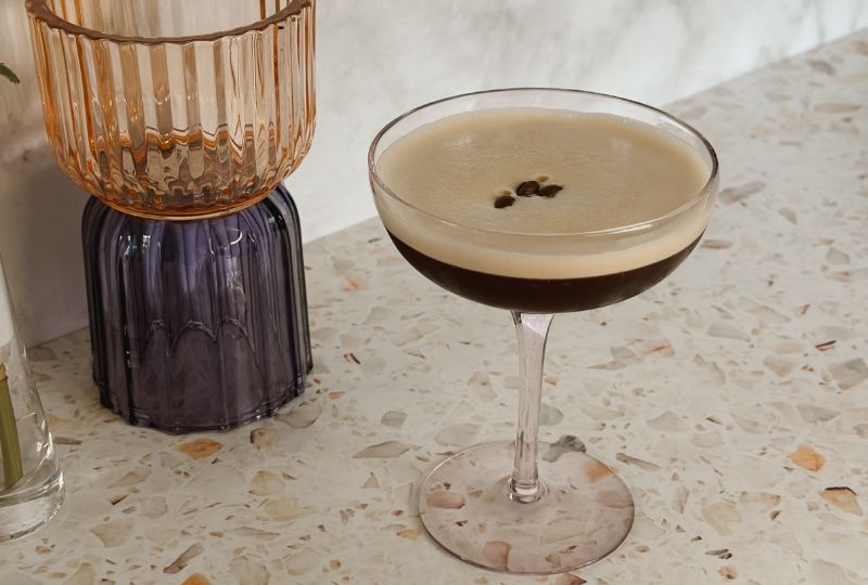 Vegan espresso martini with foam and coffee beans – cocktail on terrazzo countertop